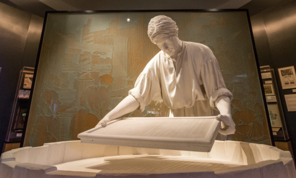 White plaster sculpture of a 17th century European papermaker at a round barrell vat