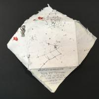 A white handmade paper envelope with black beads, bird netting, linen snippets, and black thread as inclusions. The envelope unfolds to become a square sheet of paper.