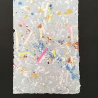  A sheet of light blue-grey handmade paper with blue, orange, and rust-colored lint, pink, green, and white office paper, and deckled edges.