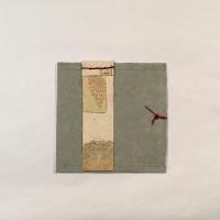 A green-grey square piece of paper with a vertical rectangle of beige paper and various cut-outs layered on top, left of the center. There is a red knot tied on the right of the piece and the beige paper is attached with red stitching.