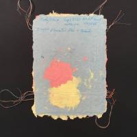 A blue piece of handmade paper with deckled edges and red and yellow patches, as well as red, blue, and yellow thread running horizontally and vertically around the border. 