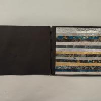 A small book of black cardstock collecting five metallic wallpaper collages and bound by hand-sewn black linen threads.  Gold, silver, blue and brown earth tones abut each other in different strata both radial and linear.