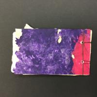 This piece is a small book with stab-binding on the left. The front cover is made from green and grey cotton pulp paint on an abaca sheet with mixed dried plant matter. The back cover is made from pink and purple poured dyed cotton pulp.