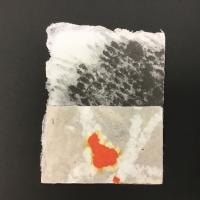 This piece is a rectangular sheet of handmade paper made from cotton rag, kozo, and mixed plant fiber with raw edges on the top and left-hand side. The bottom half of the sheet is beige and white, with an orange and yellow drop of pulp paint in the center. The top half is black, grey, and white with a seemingly-speckled texture.