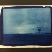 A cyanotype photographic negative in varying shades of blue printed on a sheet of Japanese Masa paper. The negative depicts a lightning storm with a birdhouse in the righthand foreground.