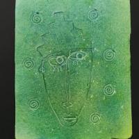 This piece is a large, green, rectangular sheet of paper with a styrofoam-like texture. Engraved in it is a stylized human face, with seven swirls bordering it.