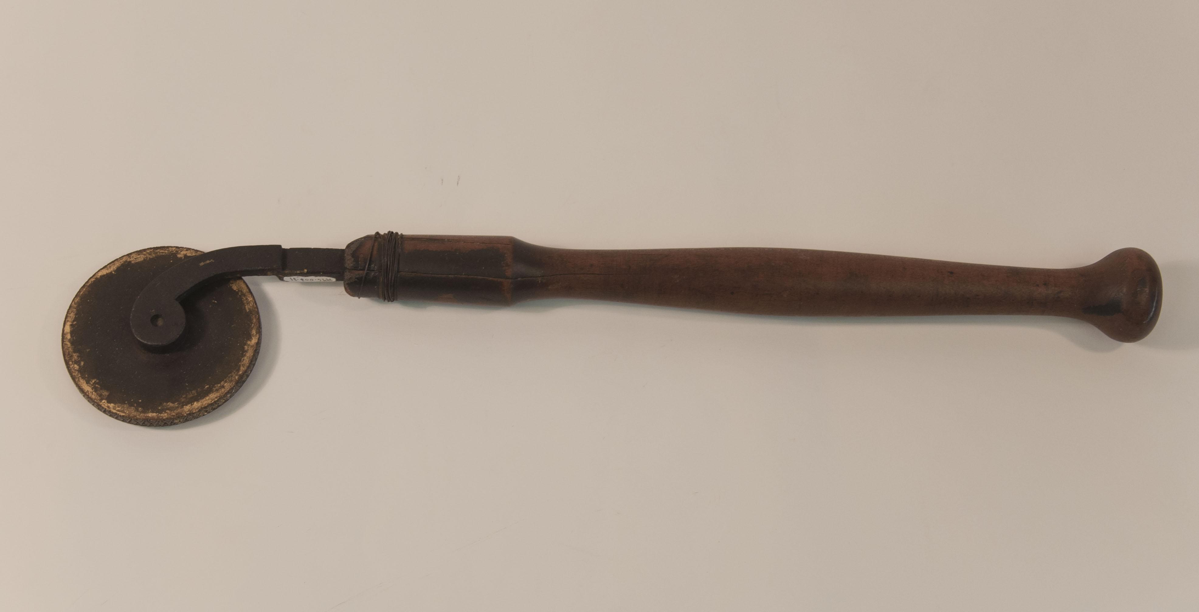 An image of the entire tool at its full length depicting its long wooden handle and round metal top