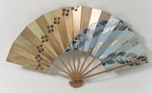 A Japanese folding fan painted gold with diamond shaped flowers painted in an arc across the fan and a baby blue stripe in the bottom right of the fan with gold flowers across